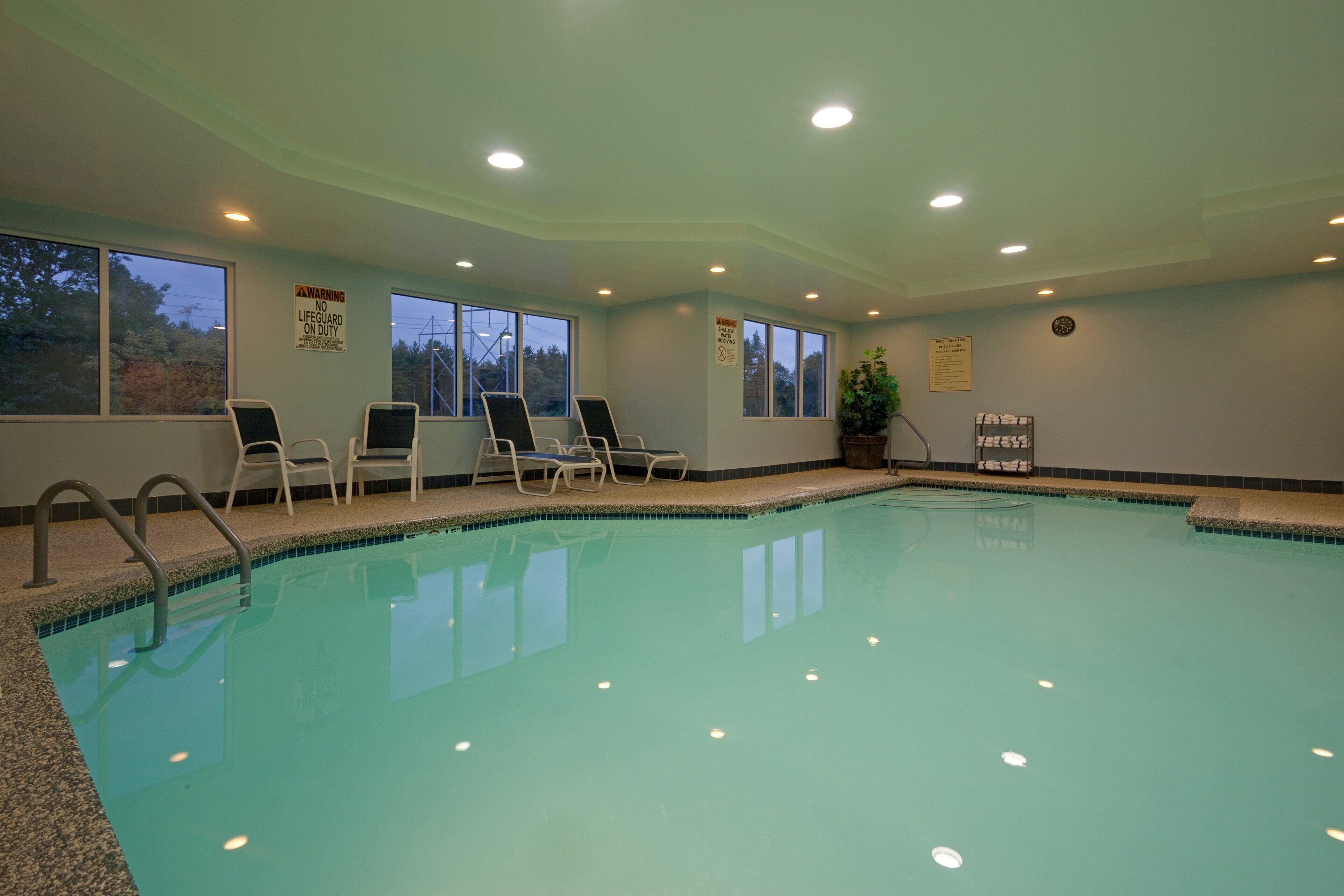 Ein Schwimmbecken mit Liegestühlen, einem Rettungsschwimmer-Schild und einem Hinweisschild für den Poolbereich.