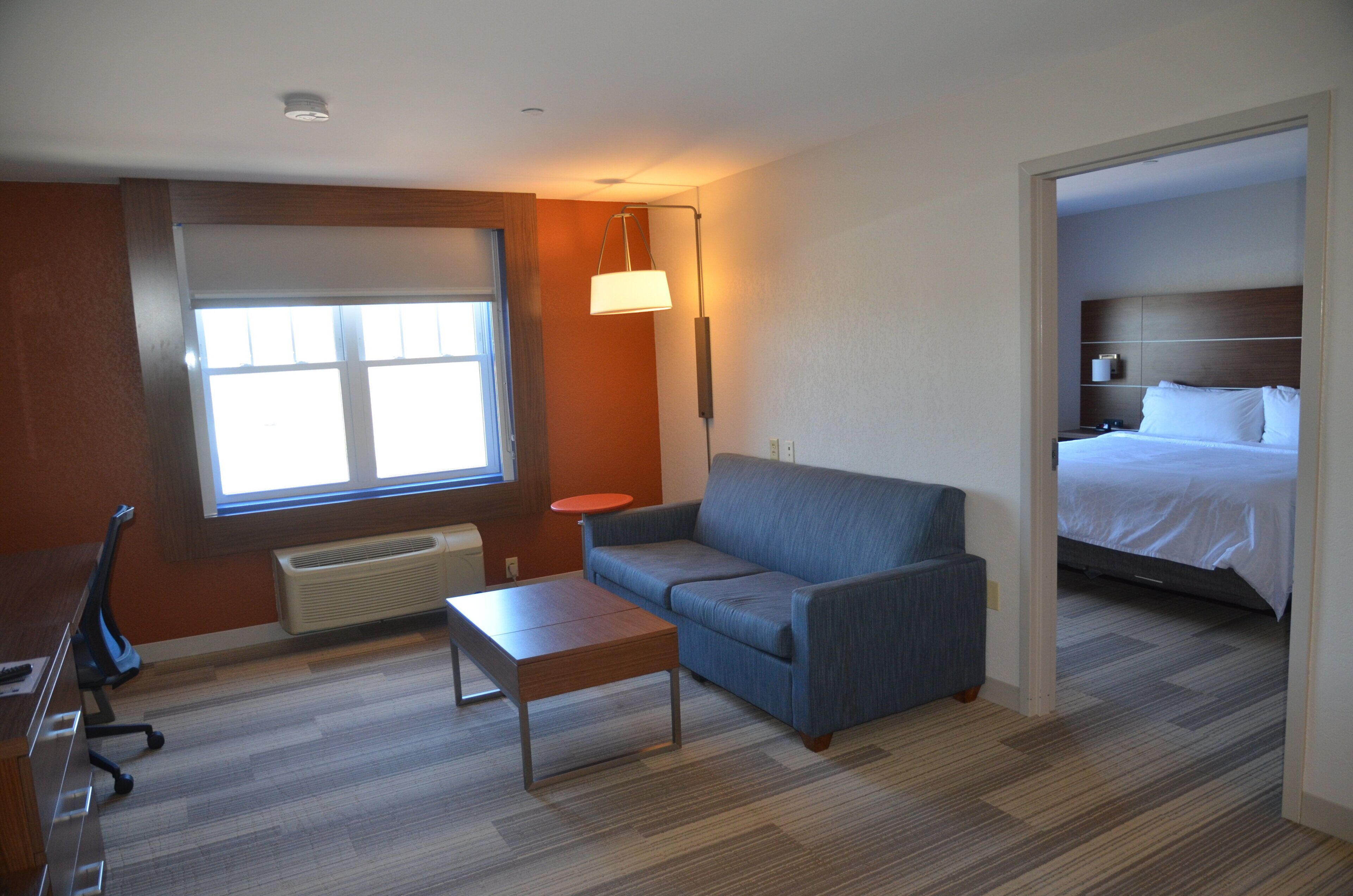 A hotel room with a bed, a sofa, a small table, a window, and a heater.