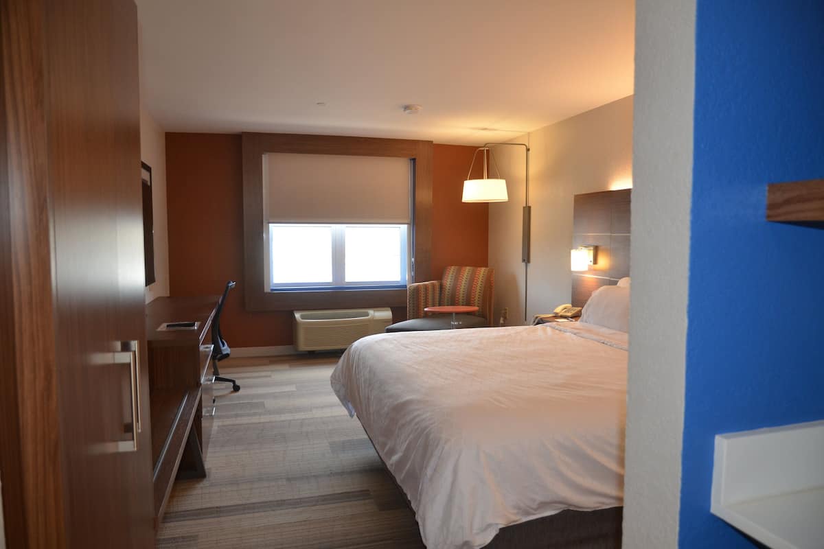 Une chambre d’hôtel équipée d’un lit, d’un bureau, d’une chaise et d’une fenêtre avec des stores.