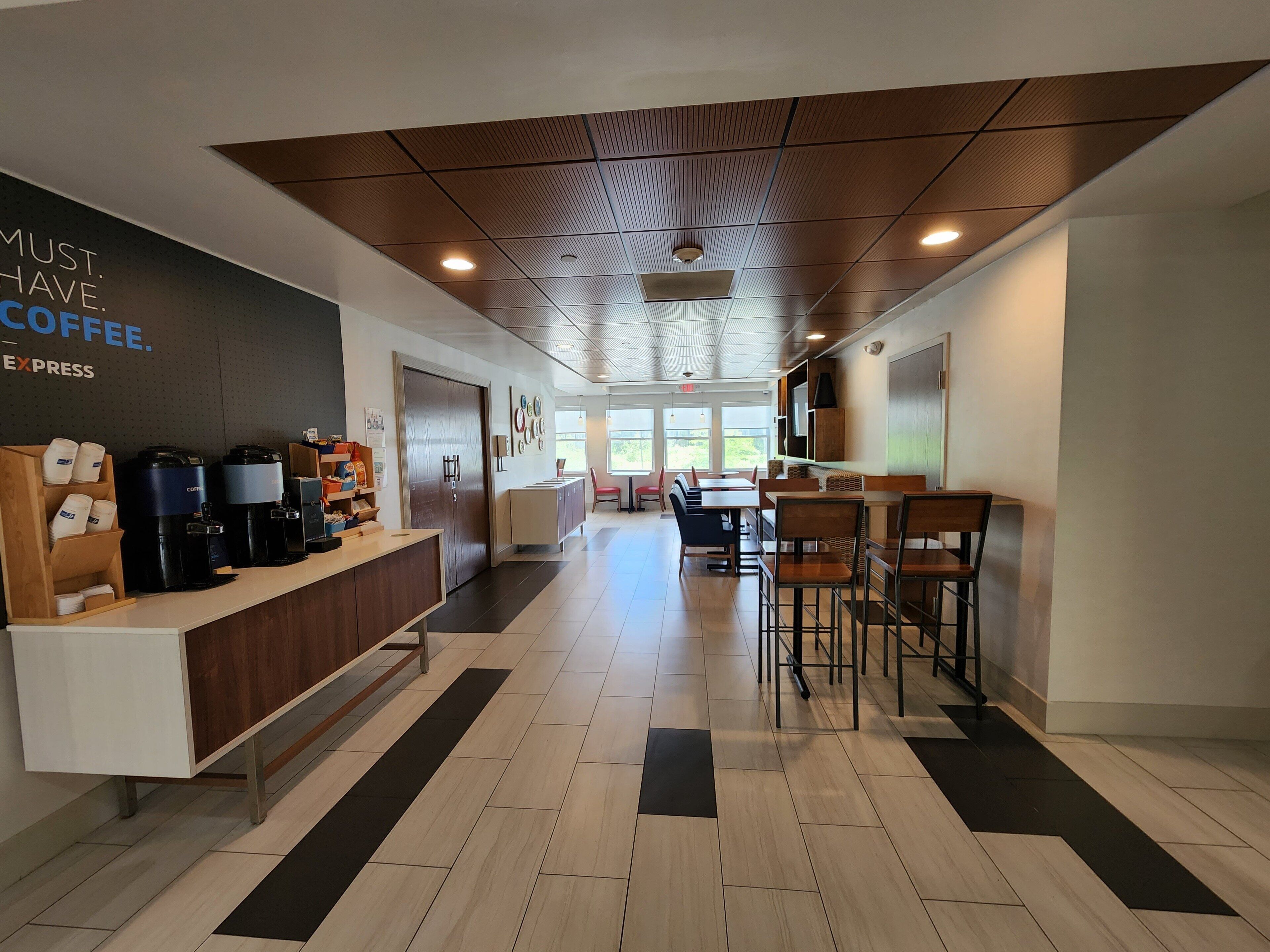 A modern coffee shop interior with a reception desk, coffee machines, seating area, and large windows.
