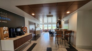 A modern coffee shop interior with a reception desk, coffee machines, seating area, and large windows. - Holiday Inn Express & Suites Rochester by IHG (Rochester)