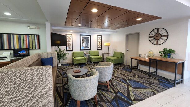 Een moderne hotellobby met een bank, groene fauteuils, een salontafel, een klok en een televisie.