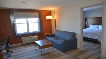 Habitación de hotel con un ventanal grande, un sofá, una mesita, una lámpara y una cama con cabecera.