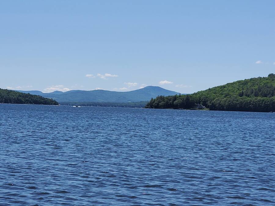 Um lago calmo com uma ilha arborizada e montanhas ao fundo.