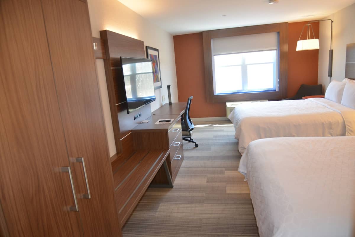 Une chambre d’hôtel avec un bureau en bois, un téléviseur à écran plat, deux lits, une grande fenêtre et une lampe fixée au mur.