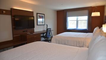 A hotel room with two beds, a desk with a chair, a television, and a window with a view.