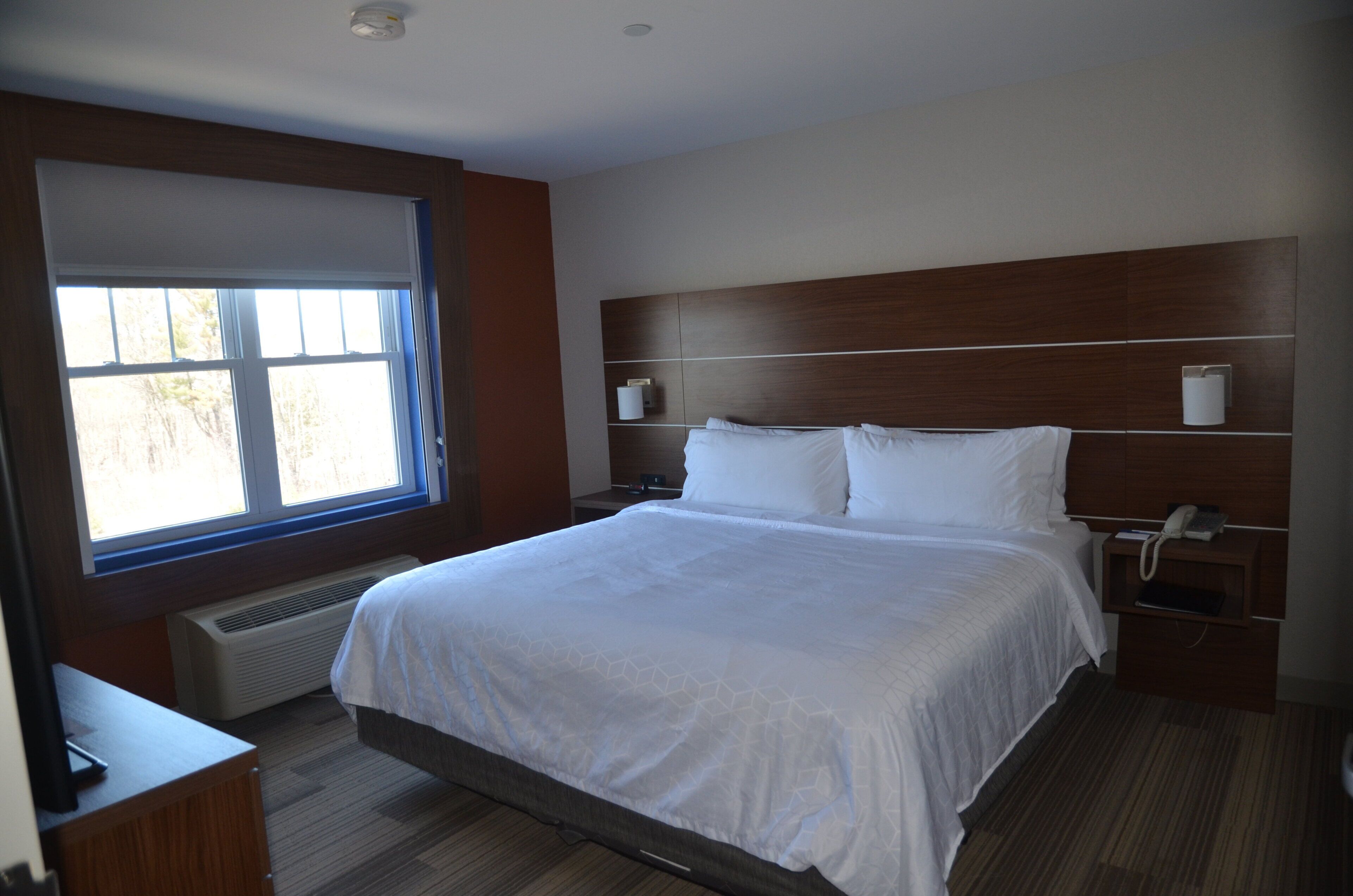 Habitación de hotel con una cama grande, una mesita de noche con teléfono, una ventana con persianas y un aplique de pared.