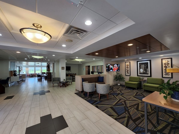 A spacious lobby with a modern design, featuring a reception desk, comfortable seating areas, and a large television screen.
