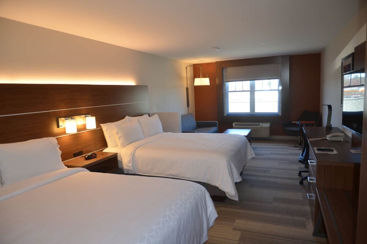 Une chambre d’hôtel avec deux lits, un bureau, une chaise, une télévision et une fenêtre avec des stores.