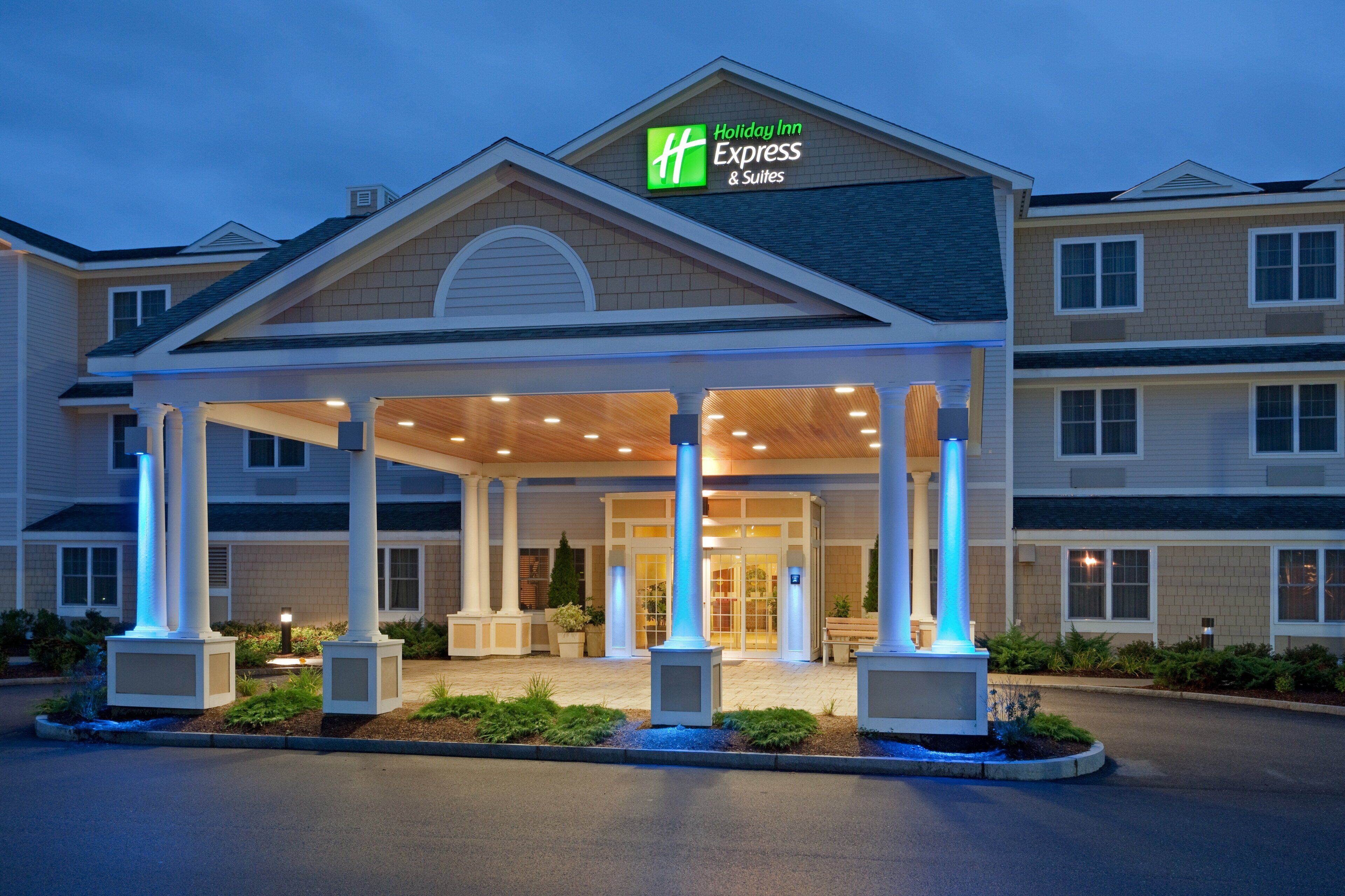 Um hotel Holiday Inn Express & Suites com entrada coberta, colunas e fachada bem iluminada.