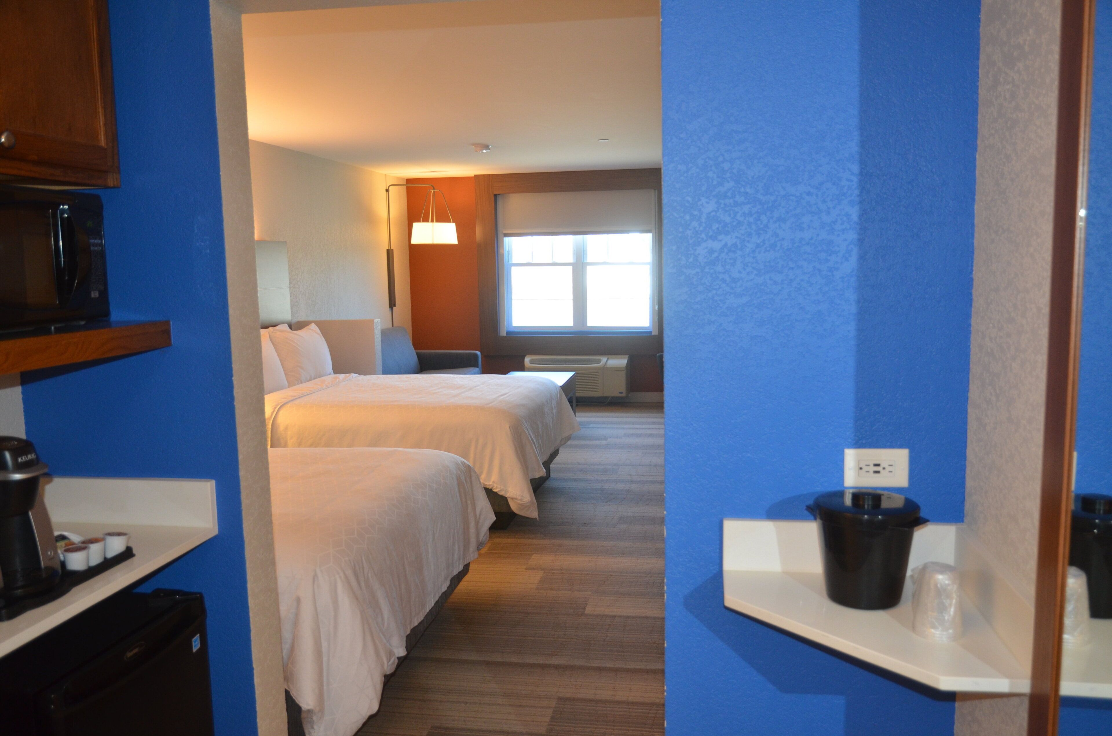 Habitación de hotel con dos camas, microondas, cafetera y ventana con persianas.