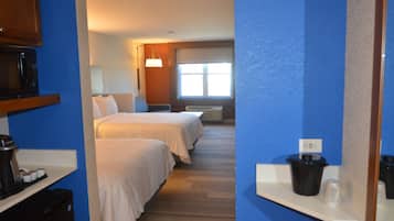 Habitación de hotel con dos camas, microondas, cafetera y ventana con persianas.