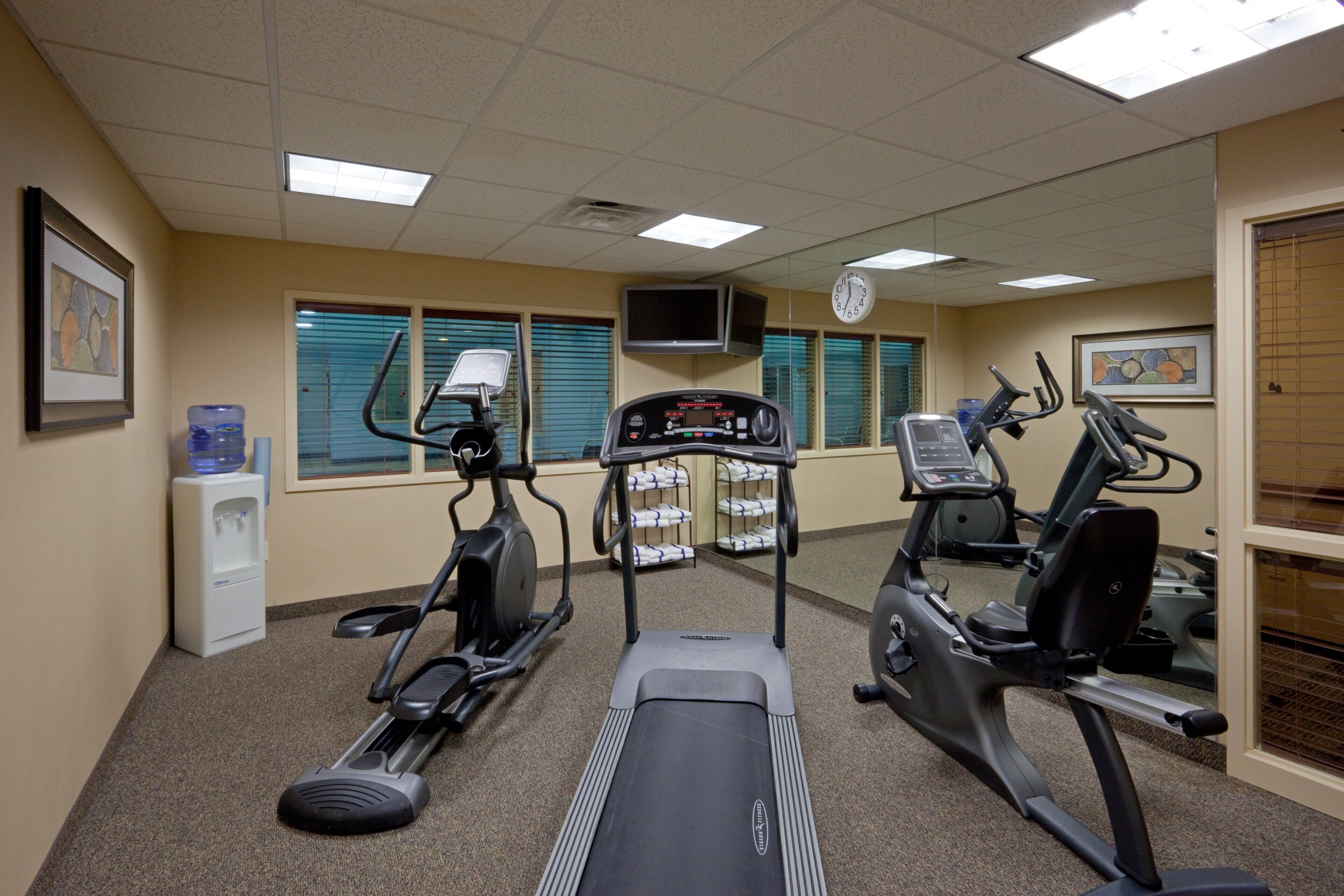 Et fitnesscenter med løbebånd, crosstrainer og en vanddispenser.