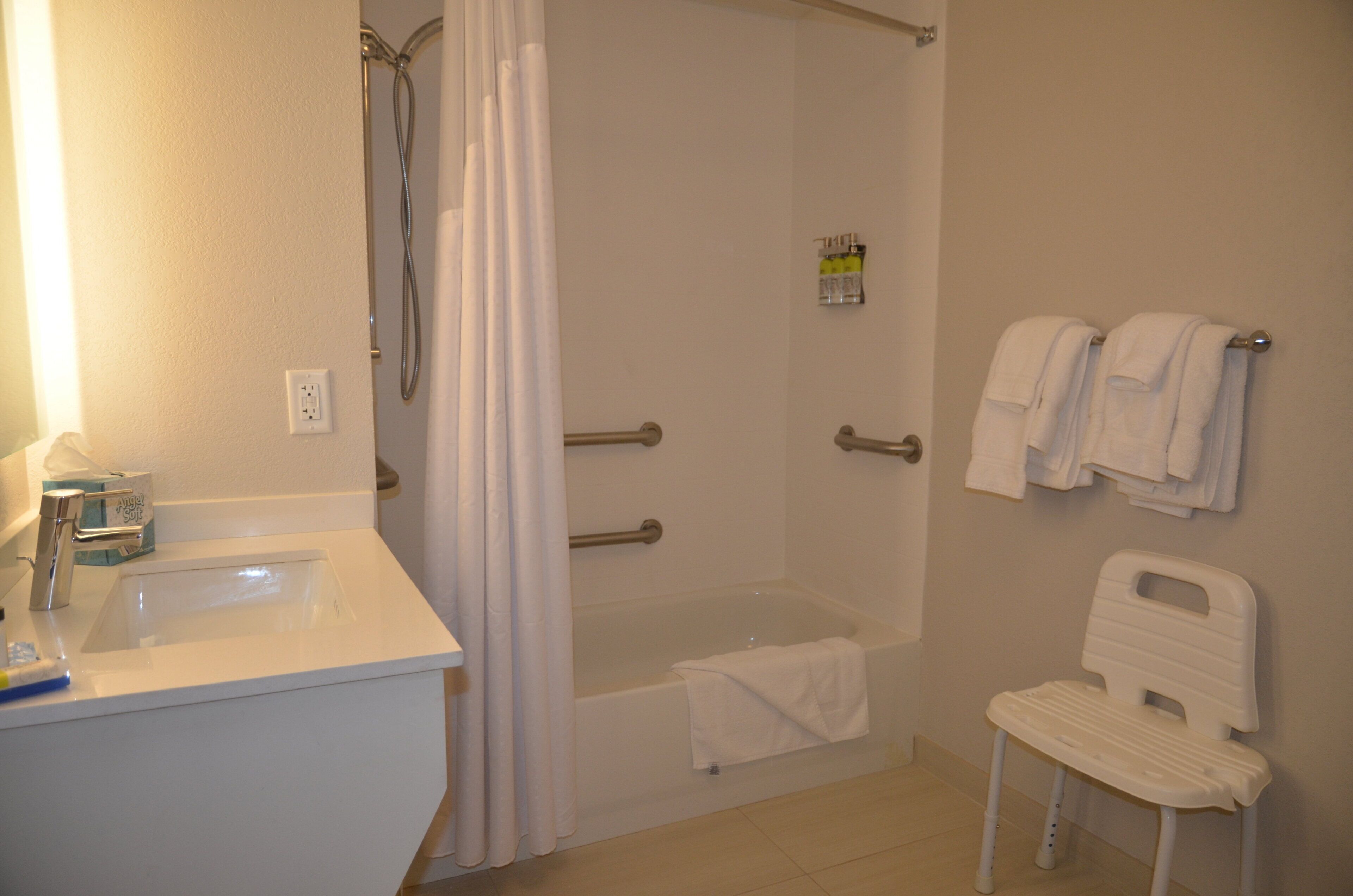 A bathroom with a shower, a sink, a toilet, and a chair.