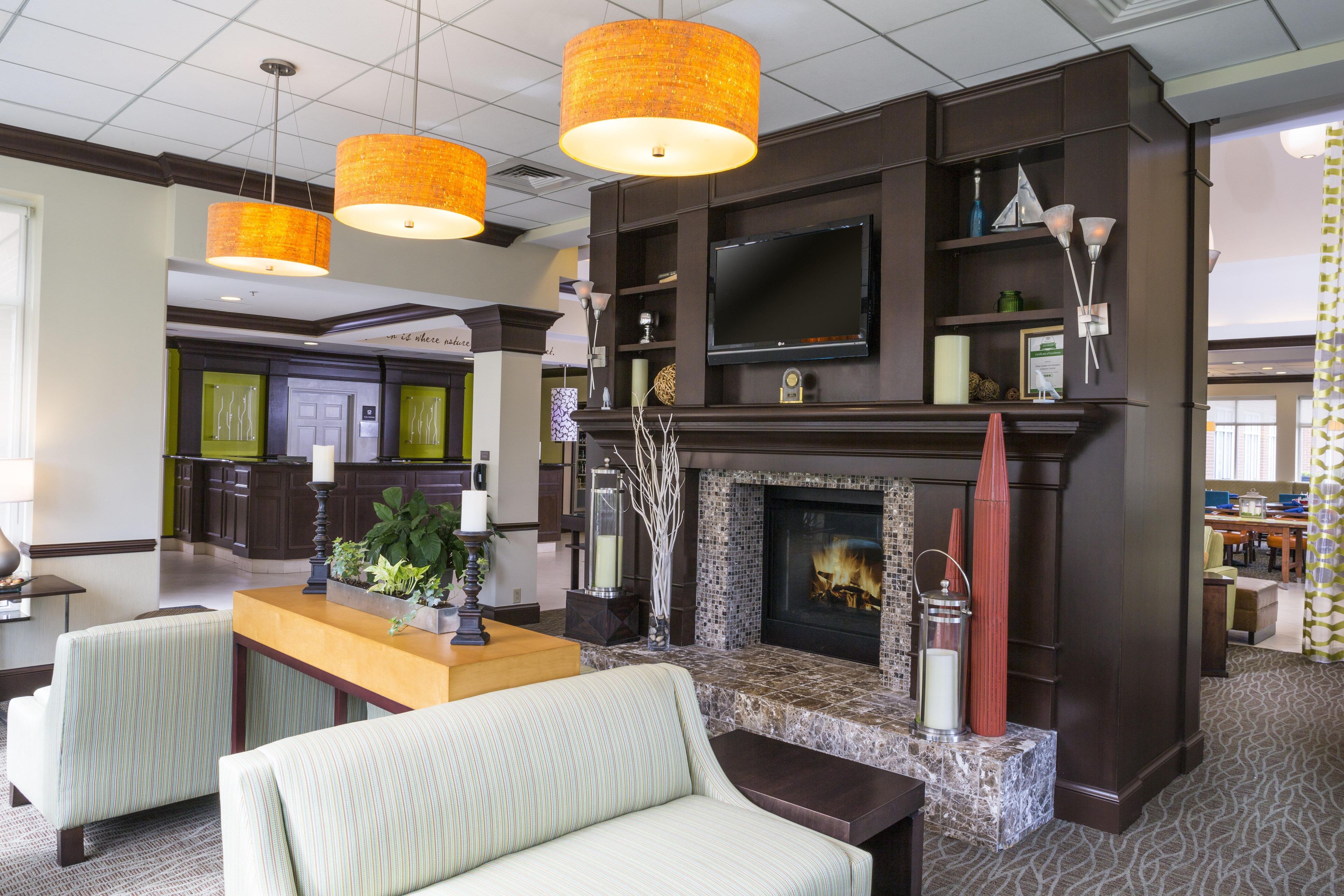 A hotel lobby with a fireplace, seating area, and a television mounted above it.