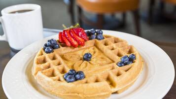 Un plato con waffles cubiertos de fresas y arándanos, una taza blanca y un fondo desenfocado.