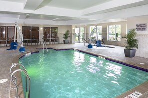 Una piscina interior con agua cristalina, un puesto de socorrista y un letrero que indica que no se permite la entrada de niños sin supervisión de un adulto.