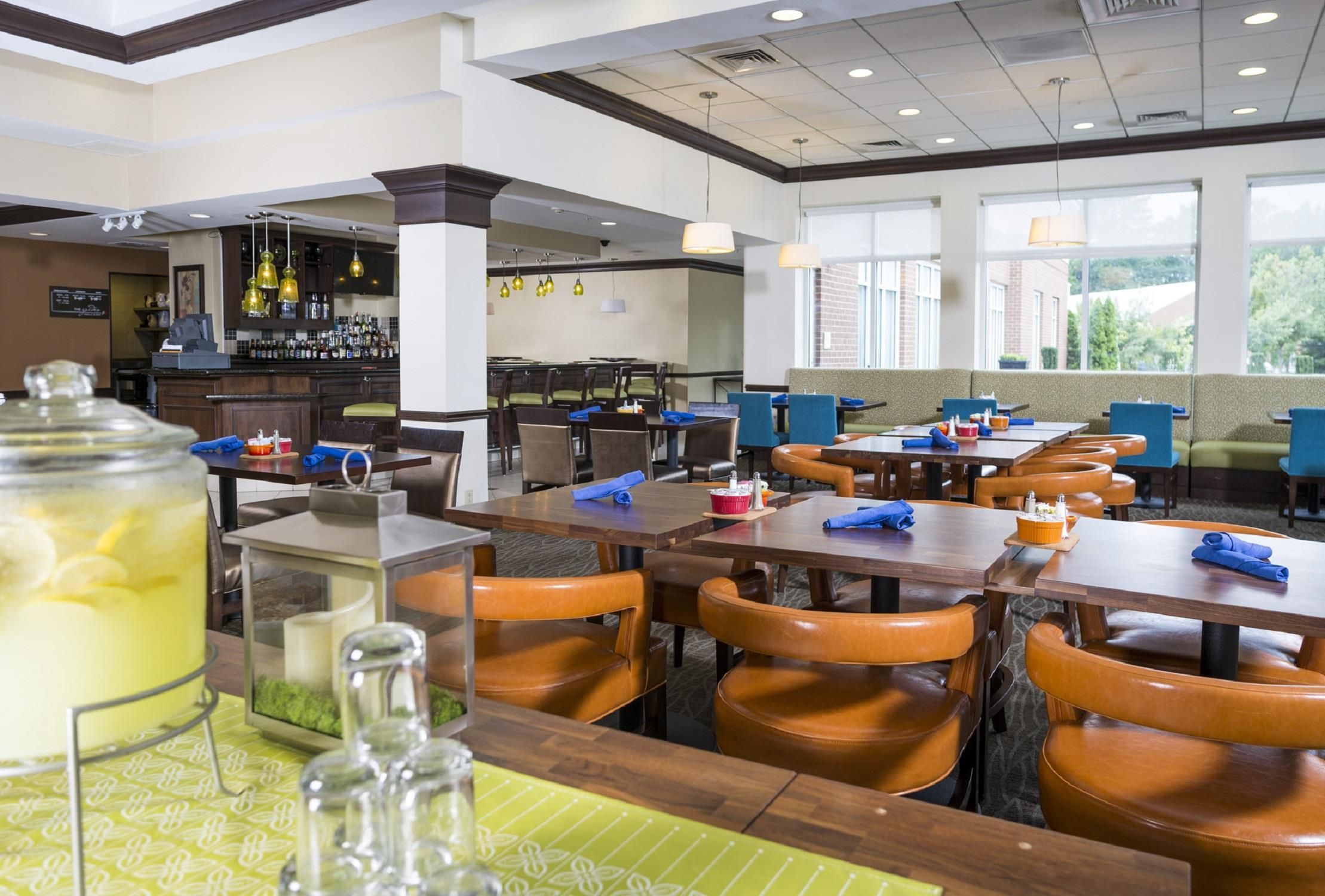 A restaurant with multiple tables and chairs, a bar area, and a large window providing a view of the outdoors.