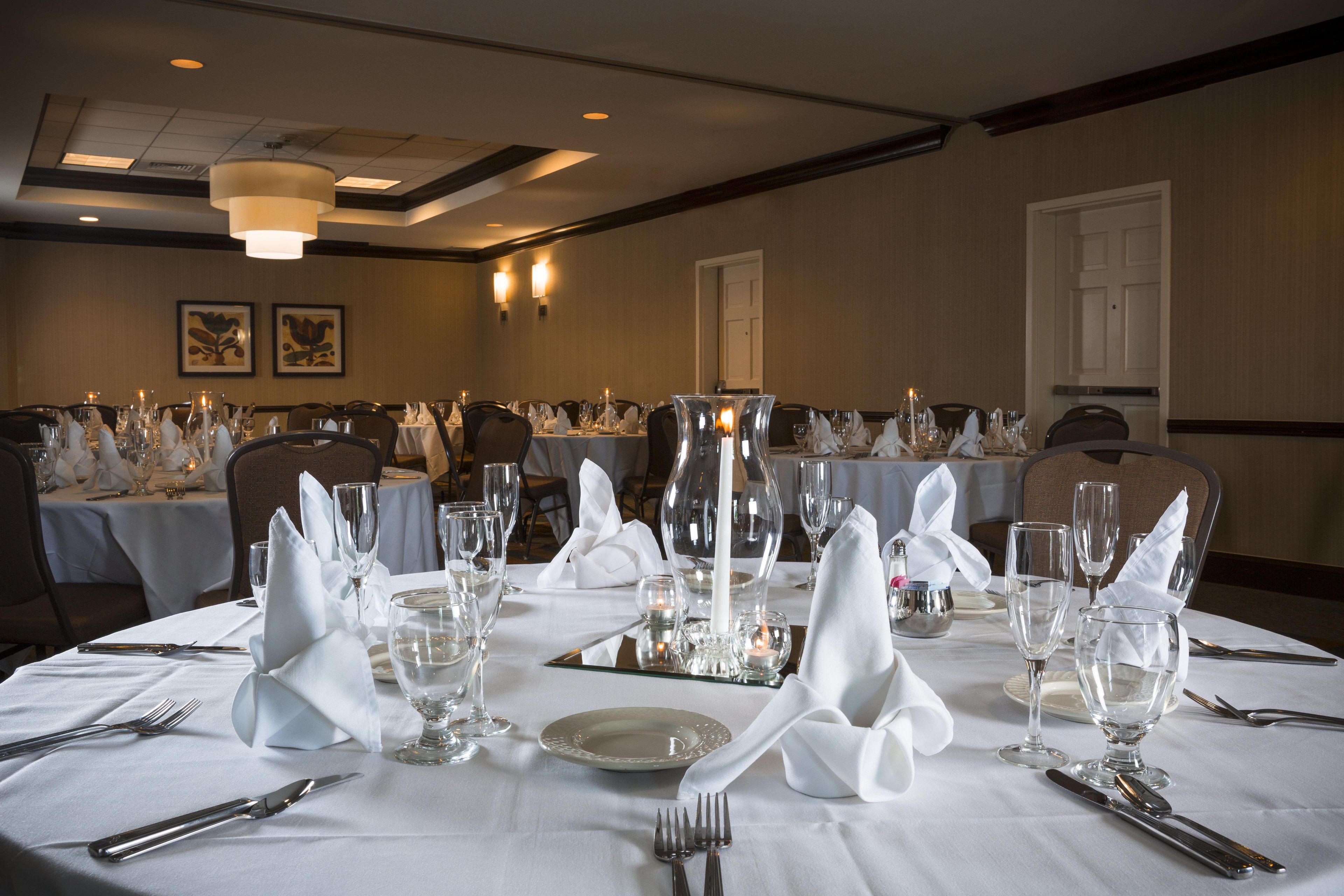 A banquet hall with round tables set for a formal event, featuring white tablecloths, glassware, and candles.