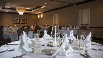 A banquet hall with round tables set for a formal event, featuring white tablecloths, glassware, and candles.
