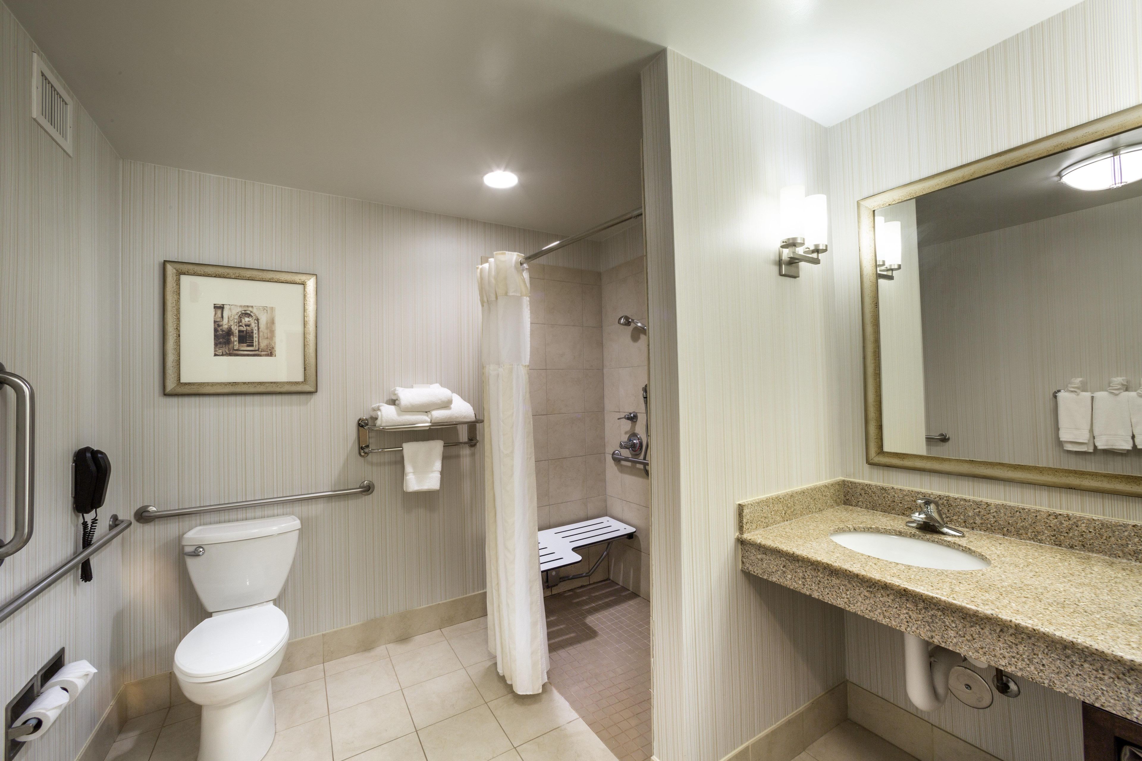 A hotel bathroom with a toilet, shower, sink, and a framed picture on the wall.