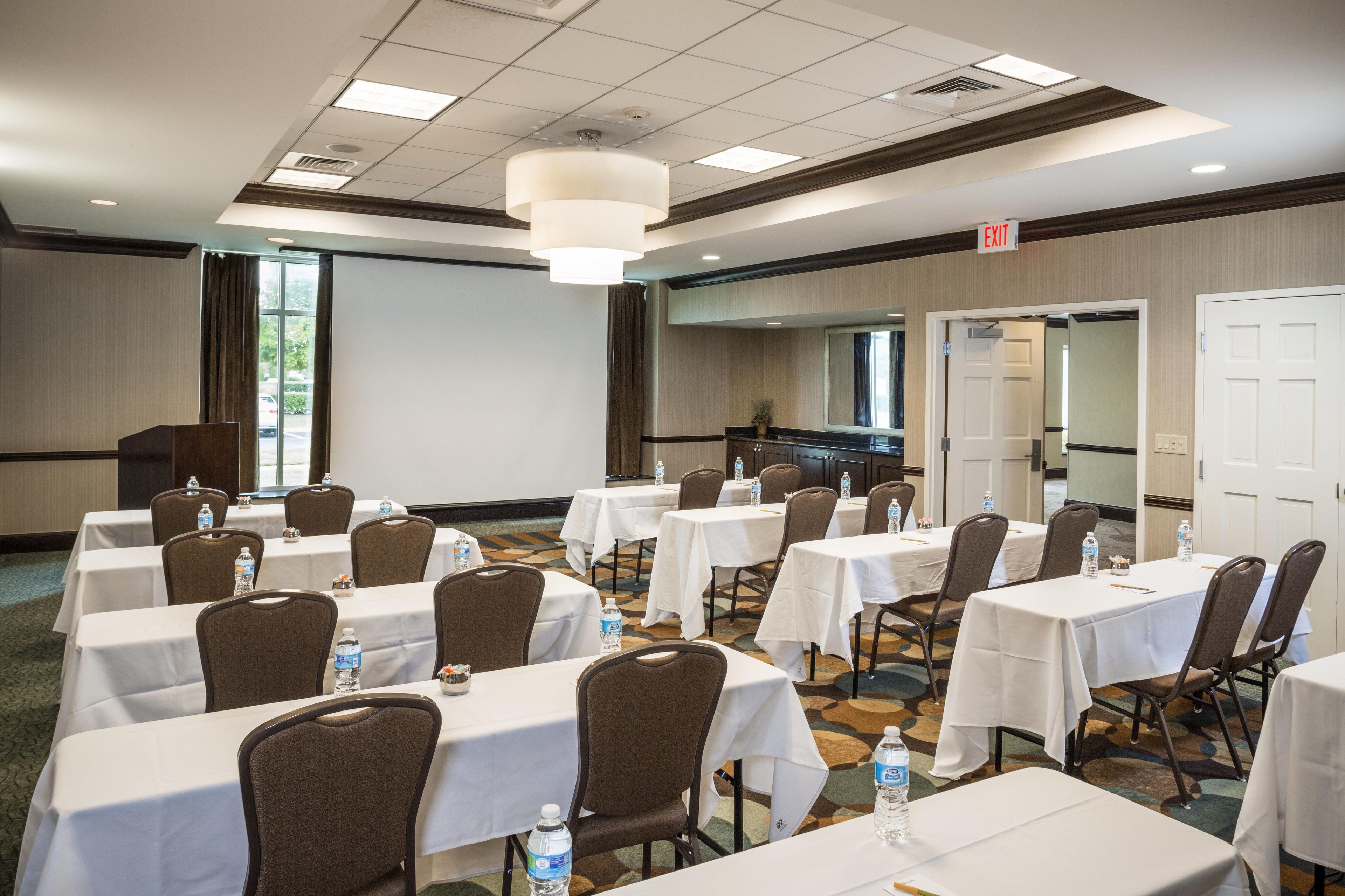 A conference room with multiple tables and chairs, equipped with water bottles, and an exit sign above a door.