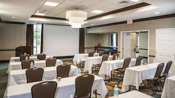 A conference room with multiple tables and chairs, equipped with water bottles, and an exit sign above a door.
