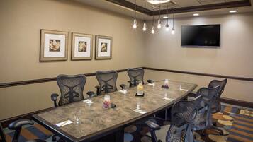 A conference room with a long table, six chairs, a TV on the wall, and framed floral artwork.