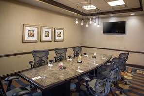 A conference room with a long table, six chairs, a TV on the wall, and framed floral artwork. - Hilton Garden Inn Hampton Coliseum Central (Hampton)