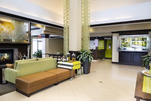 A lobby with a sofa, a fireplace, a bar area, and a large window. - Hilton Garden Inn Hampton Coliseum Central (Hampton)