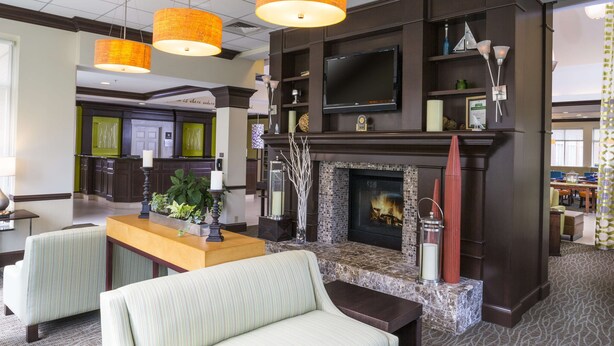 A hotel lobby with a fireplace, seating area, and a television mounted on the wall. - Hilton Garden Inn Hampton Coliseum Central (Hampton)