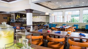 A hotel dining area with multiple tables and chairs, a bar area, and large windows offering a view. - Hilton Garden Inn Hampton Coliseum Central (Hampton)
