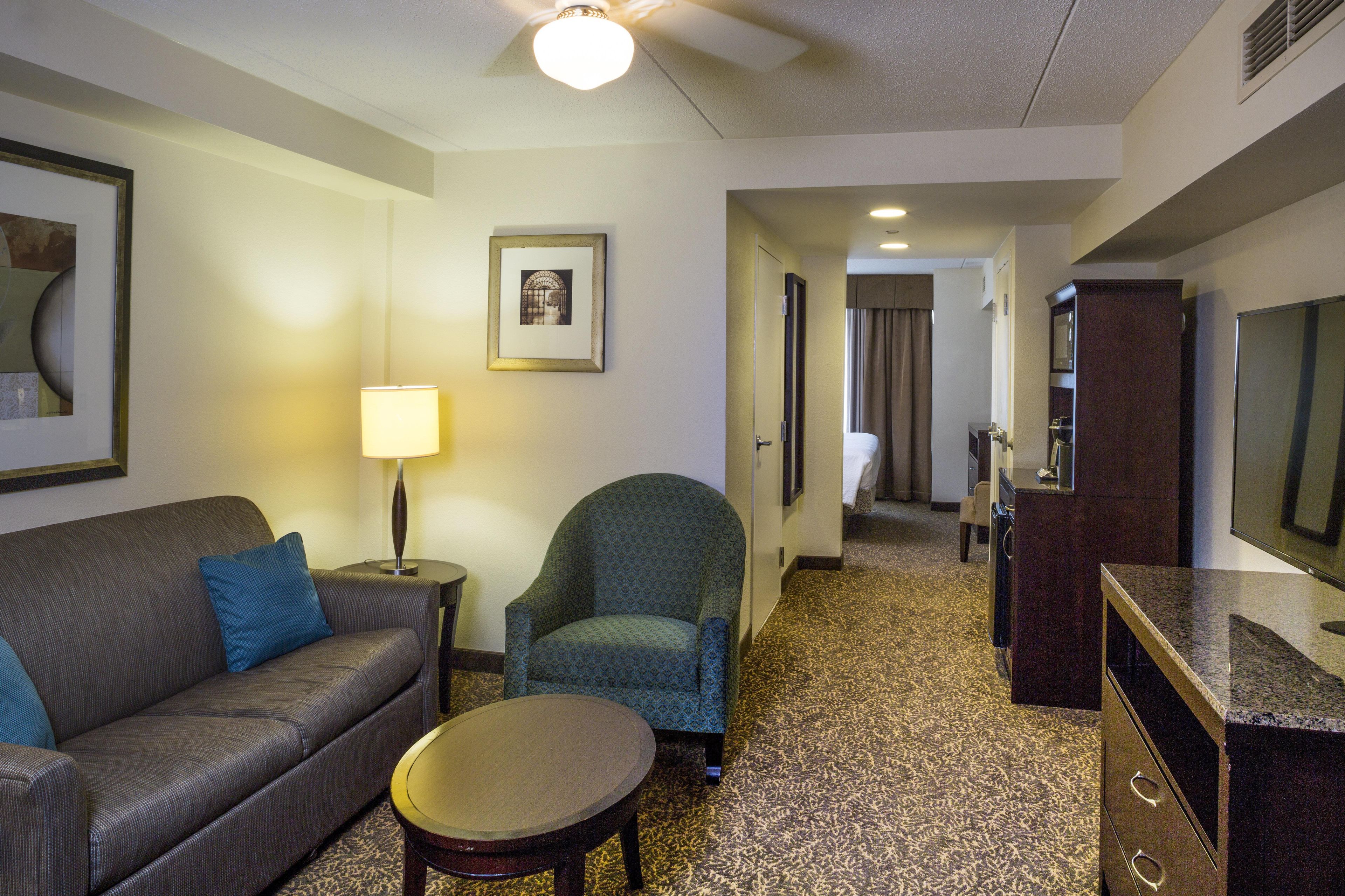 A hotel room with a sofa, armchair, small table, lamp, and a television.