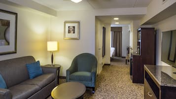 A hotel room with a sofa, armchair, small table, lamp, and a television.