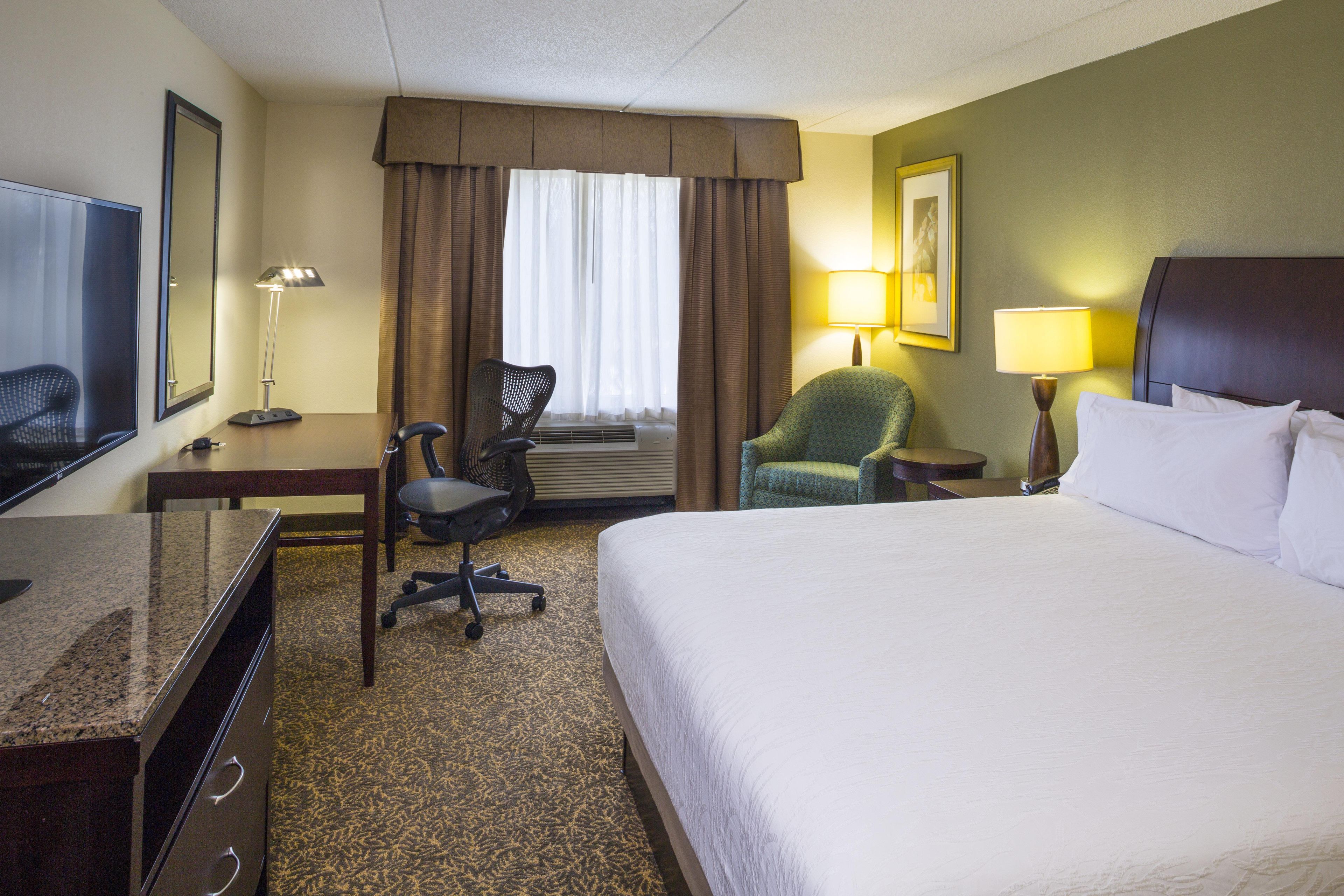 A hotel room with a bed, desk, chair, and a television.
