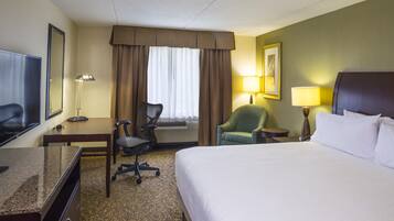 A hotel room with a bed, desk, chair, and a television.