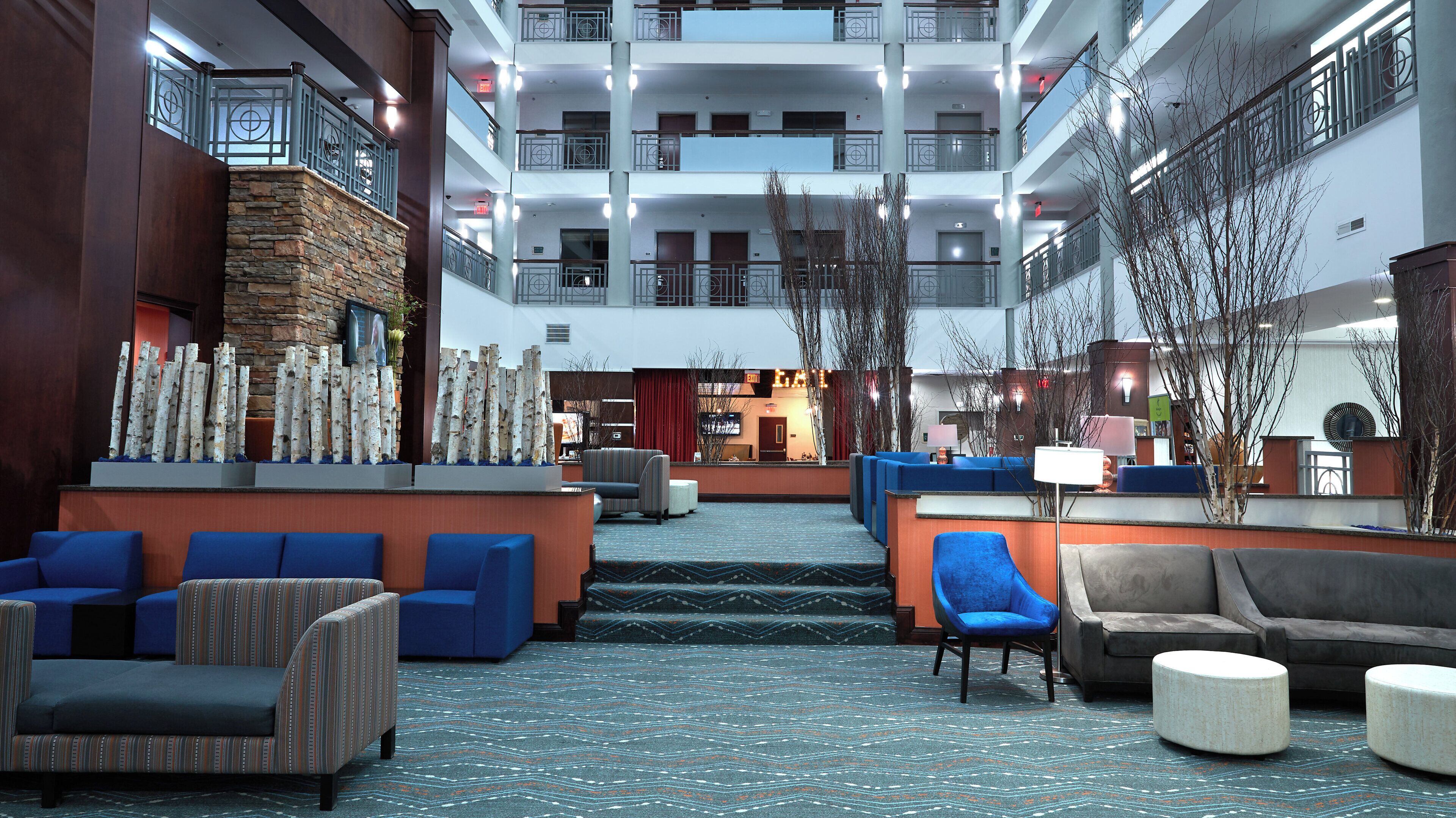 A hotel lobby with a central seating area, a reception desk, and a view of the building's exterior.