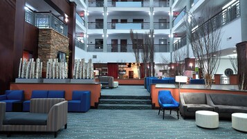Um hall de hotel com área de estar central, balcão de recepção e vista para o exterior do edifício.