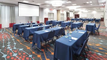 Un salón de conferencias con varias mesas, sillas y una pantalla grande.