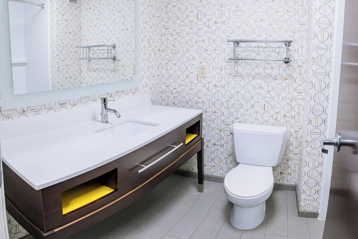 A modern bathroom with a white sink, a mirror, a toilet, and patterned wallpaper.