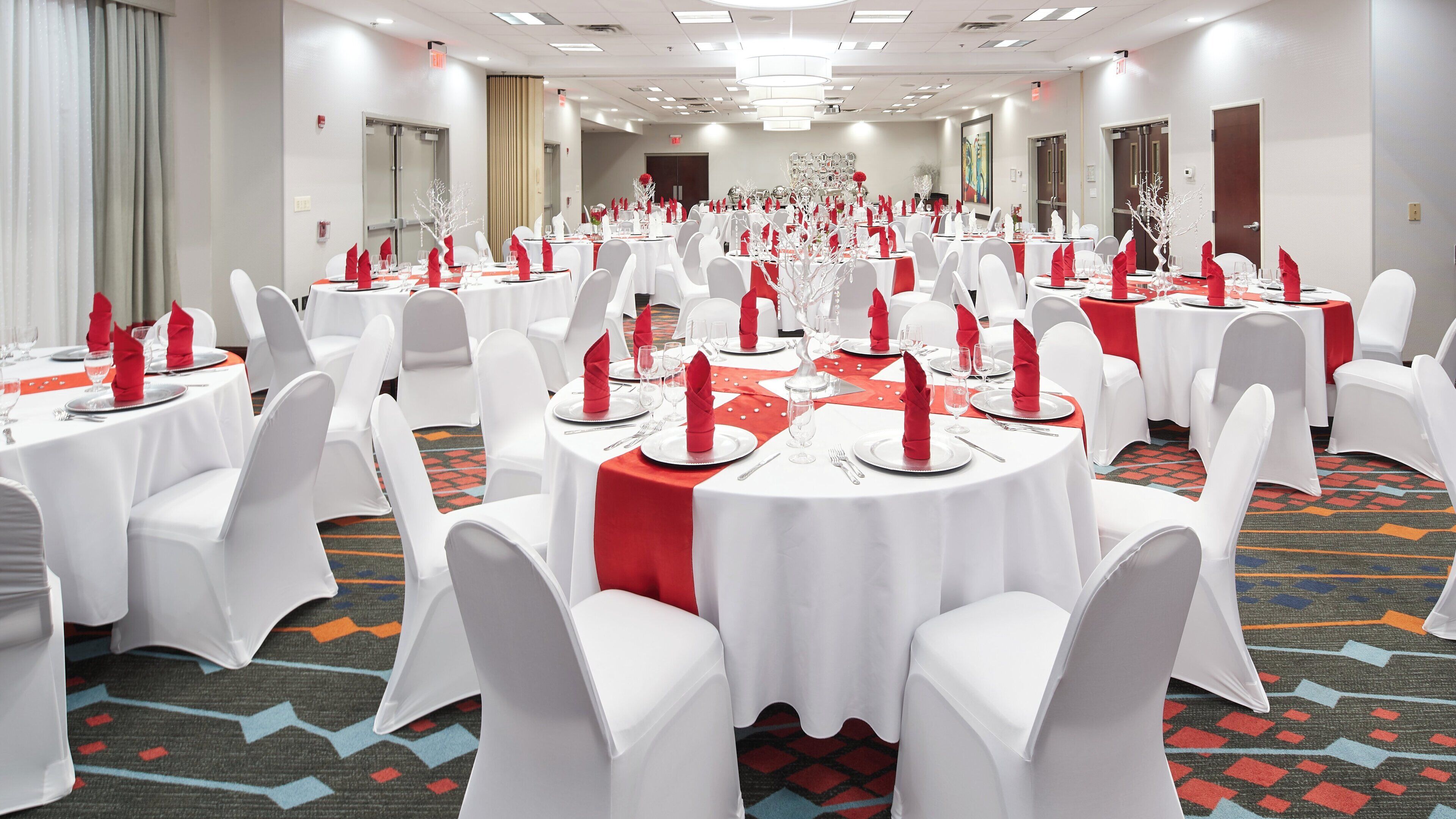 A banquet hall with round tables, white chairs, and red napkins.