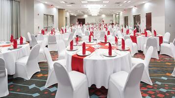 A banquet hall with round tables, white chairs, and red napkins.