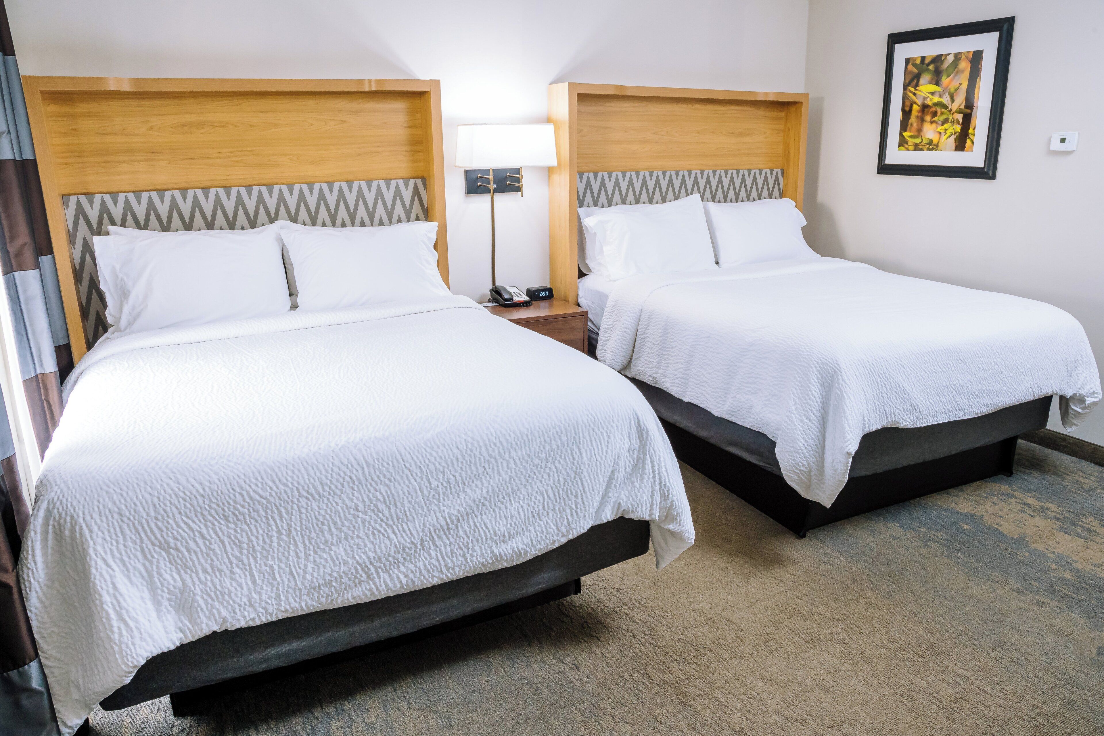 A hotel room with two beds, a nightstand with a lamp, and a framed picture on the wall.