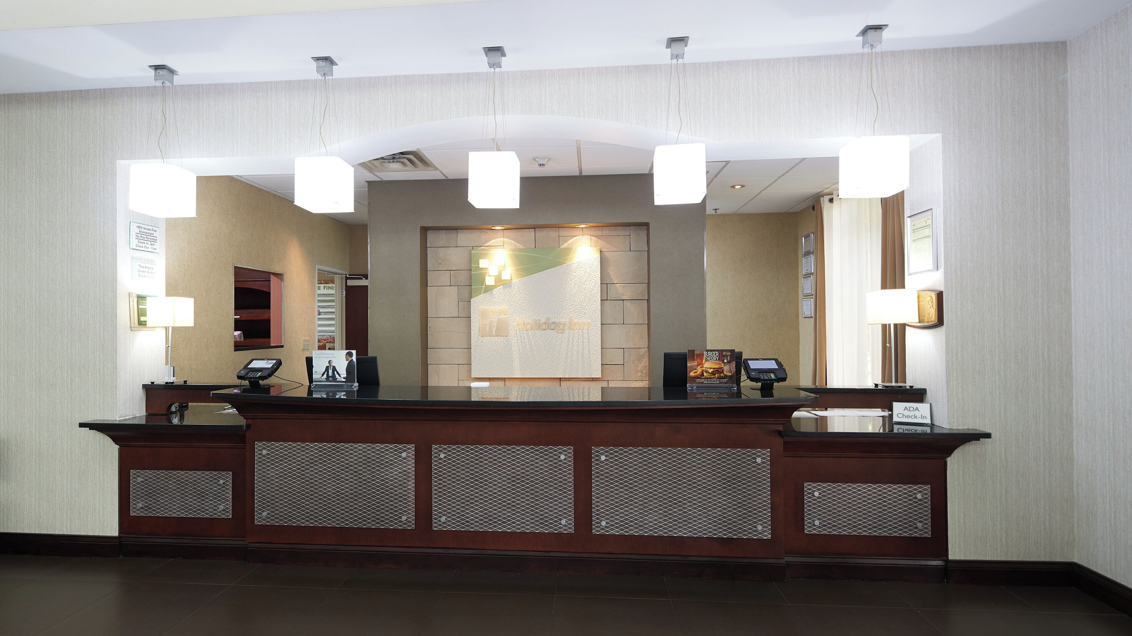 A hotel reception desk with a check-in counter, a digital display, and a reception area with a wall-mounted sign.