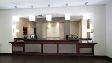 A hotel reception desk with a check-in counter, a digital display, and a reception area with a wall-mounted sign.