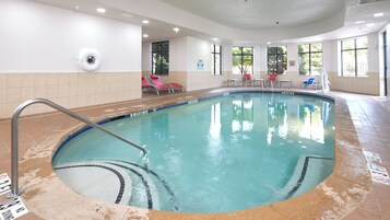 An indoor swimming pool with a diving board, poolside chairs, and a lifeguard chair.