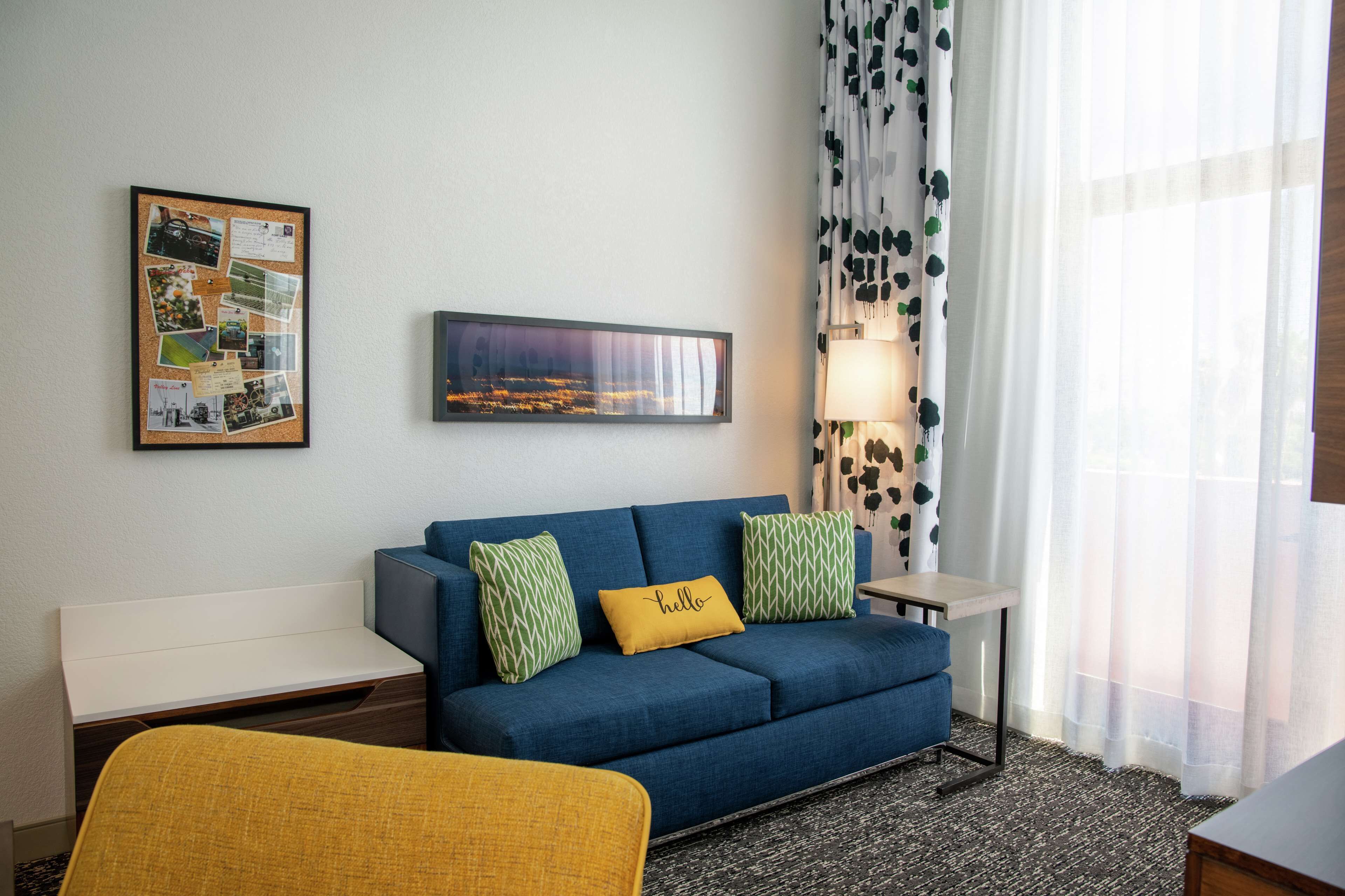 A room with a blue sofa, a yellow chair, a framed collage on the wall, and a lamp near the window.