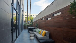 A narrow outdoor corridor with a modern grey sofa, black and white chairs, and a small round table. - Hampton Inn & Suites Los Angeles/Sherman Oaks (Van Nuys)