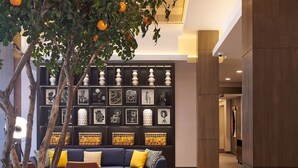 A modern lobby with a geometric patterned floor, a seating area with sofas and chairs, a wall with framed artwork, and a tree with oranges. - Hampton Inn & Suites Los Angeles/Sherman Oaks (Van Nuys)