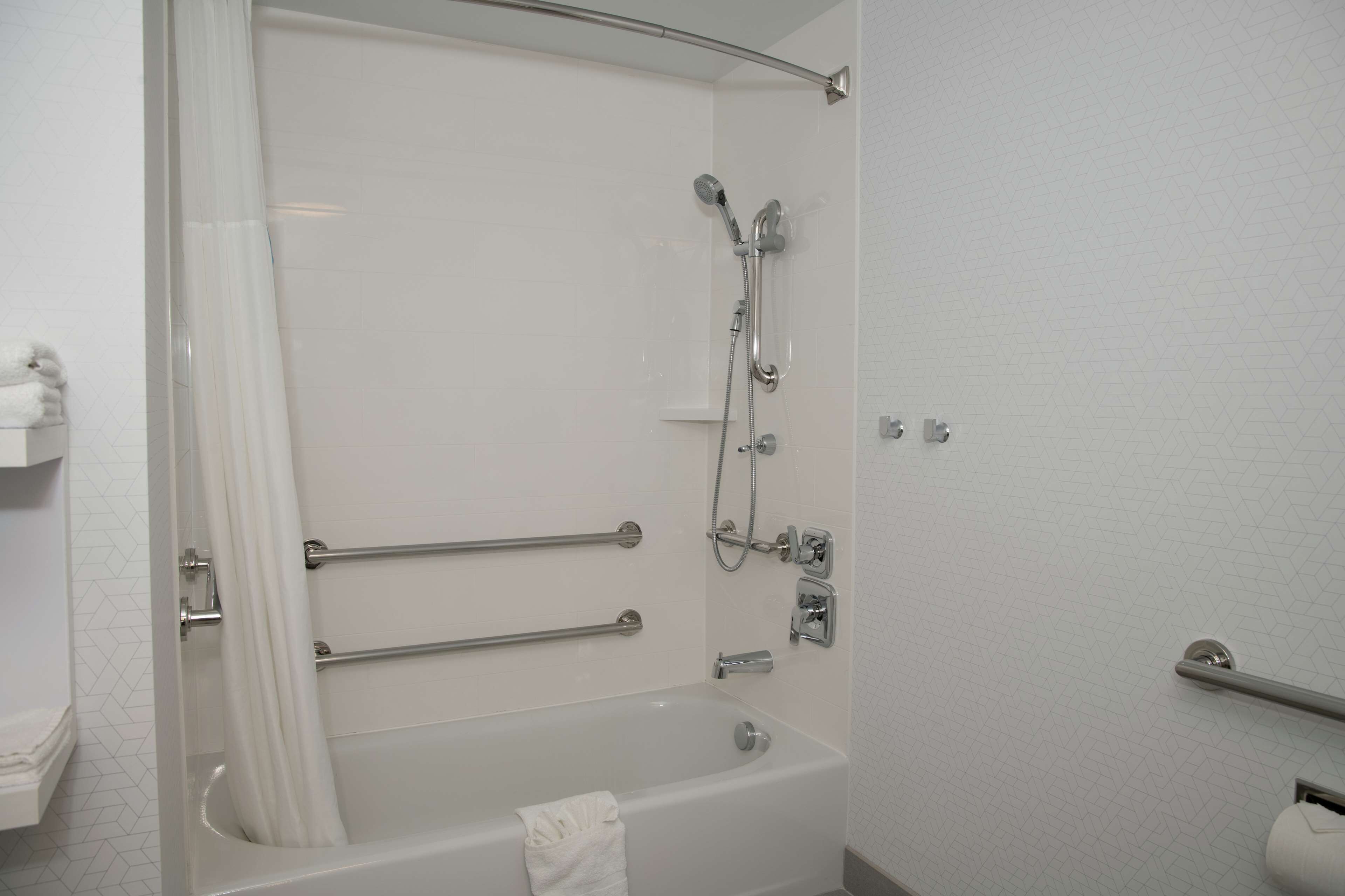A modern bathroom with a bathtub, shower, and grab bars.